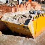 Photo of an yellow rubbish container at a construction site.